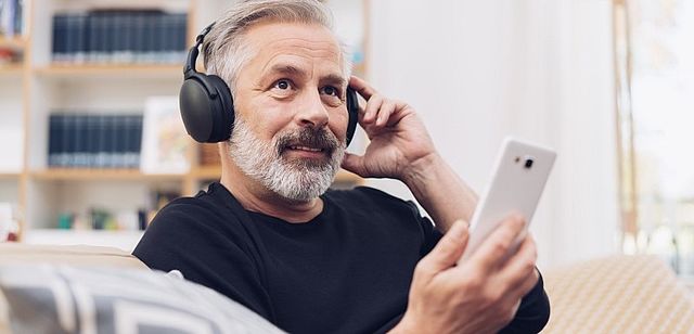 Mann mittleren Alters welcher auf der Couch Podcasts hört