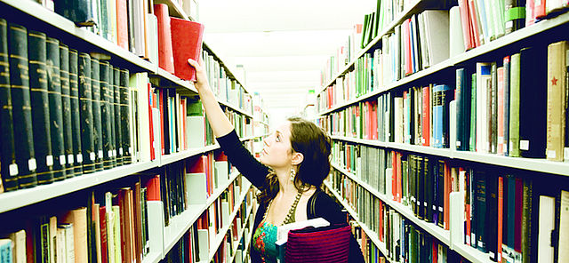 Junge Frau nimmt in Bibliothek Buch aus Bücherregal