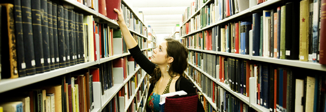 Junge Frau nimmt sich in der Bibliothek ein Buch